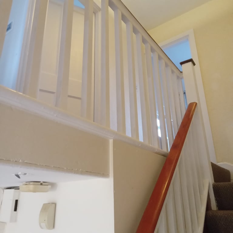 White stair railing and banister in a hallway with yellow walls, light fixtures, and a red handrail visible on the right side